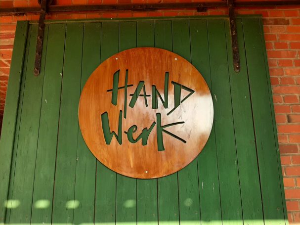 Holzschild mit der Aufschrift „HANDWERK“ auf grünem Hintergrund.